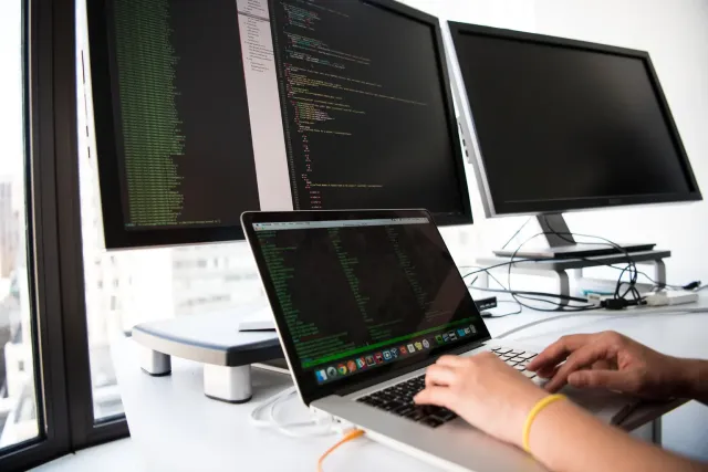 A desk with a laptop, a short checklist and two hands shaking over a code window