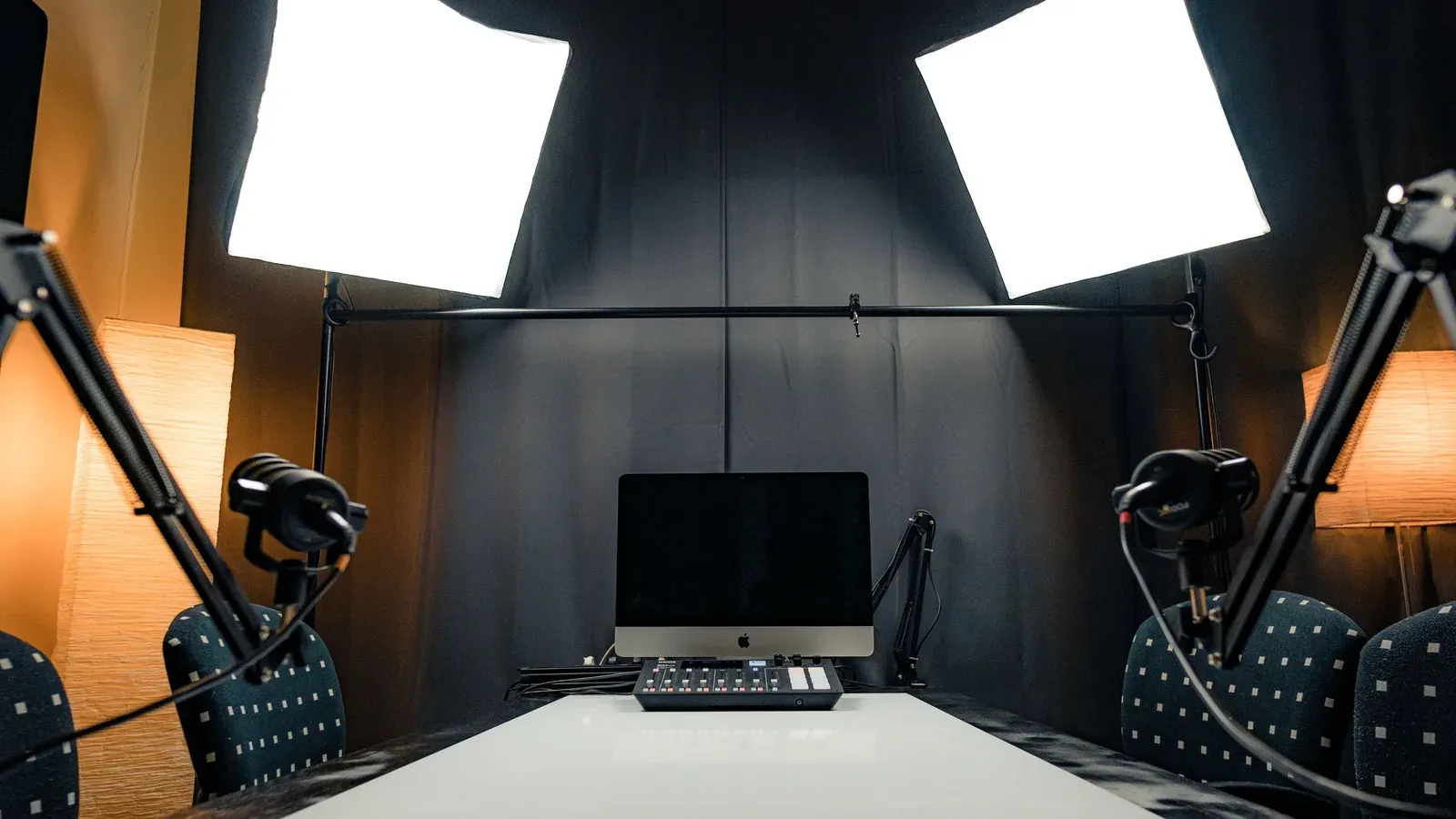 A minimal podcast desk with microphone, headphones, laptop and plant
